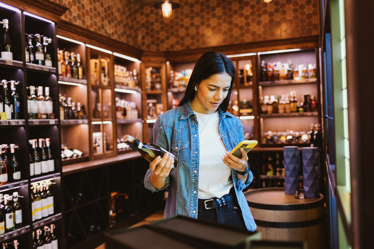 Woman with Phone Choosing Liquor in the Store